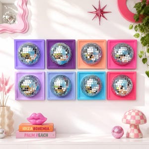 May include: Eight square wall art pieces, each featuring a central silver mirrored disco ball mounted on a solid-colored frame in shades of purple, orange, pink, and blue. The frames are arranged in two rows of four on a white wall.