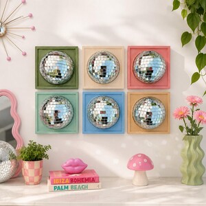 Pode incluir: Uma decora&ccedil;&atilde;o de parede com seis molduras quadradas, cada uma contendo uma bola de discoteca prateada. As molduras s&atilde;o pintadas em verde-oliva, creme, coral, verde-menta, azul-claro e bege. O arranjo forma uma grade de duas linhas e tr&ecirc;s colunas.