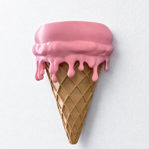 May include: A wall-mounted sculpture shaped like an ice cream cone with a tan, waffle-textured base and a large scoop of smooth, pink ice cream on top. The pink ice cream features realistic drips cascading down the sides of the cone.