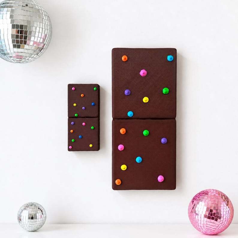 May include: Two rectangular brown wall art pieces resembling chocolate brownies, each decorated with small, raised, multi-colored dots in shades of pink, yellow, blue, orange, purple, and green, accompanied by two silver and one pink disco ball.