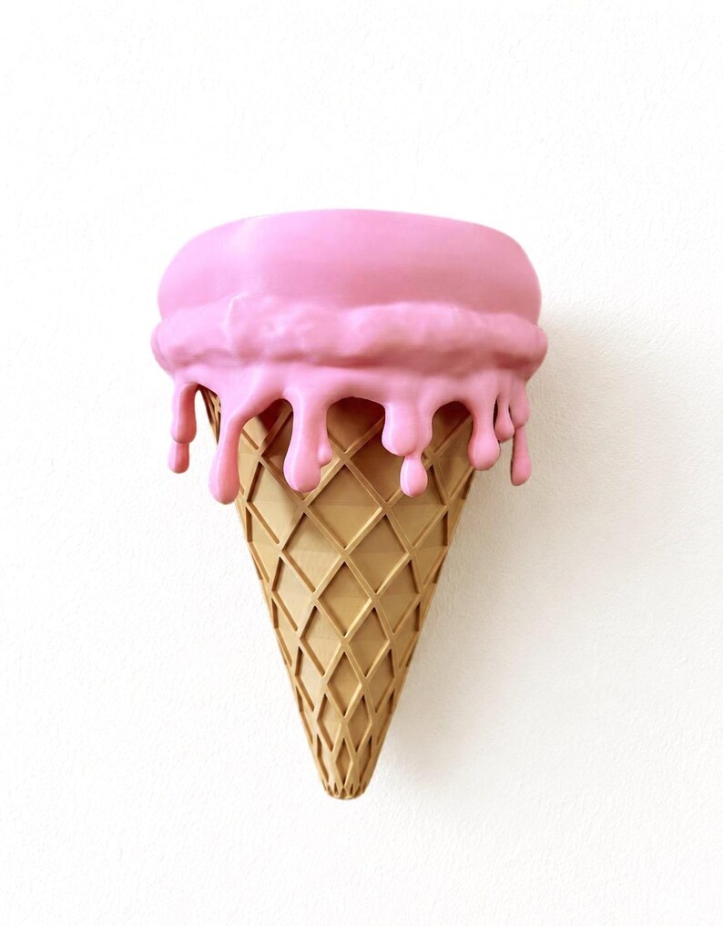 May include: A wall-mounted sculpture shaped like an ice cream cone with a tan, diamond-patterned waffle cone base and a large, rounded scoop of pink ice cream on top, featuring thick, realistic drips cascading down the sides of the cone.