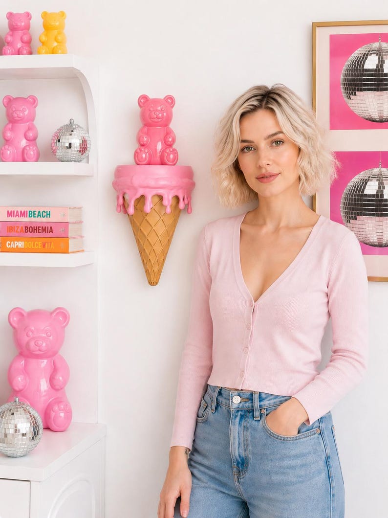 May include: A light pink long-sleeve button-down cardigan paired with light blue denim jeans. The cardigan features a V-neckline and a ribbed knit texture, worn with a simple, clean aesthetic that complements the surrounding decor.
