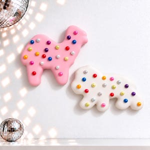 May include: A pink camel-shaped wall decoration and a white dog-shaped wall decoration, both featuring scattered multicolored spherical beads across their surfaces. The items are displayed against a plain white wall with disco ball reflections.