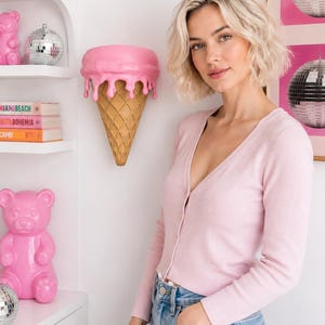May include: A light pink long-sleeve cardigan with a V-neckline and a ribbed texture, worn with blue denim jeans. The cardigan features a button-down front closure and a fitted silhouette that reaches the waistline, providing a simple look.