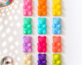 May include: A collection of twelve gummy bear-shaped figures arranged in a grid. The figures are rendered in various solid colors including pink, orange, yellow, teal, light blue, purple, magenta, coral, cream, dark purple, and lime green.