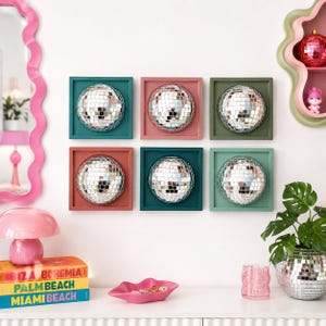 May include: Six square wall art pieces, each featuring a centered silver mirrored disco ball. The frames are painted in various solid colors including teal, pink, olive green, terracotta, dark blue, and light green, arranged in a two-by-three grid.