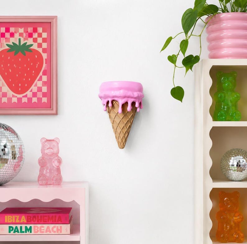 May include: A wall-mounted pink ice cream cone sculpture with a textured waffle pattern. The top section features a smooth, bright pink scoop with realistic drips cascading down the sides, creating a playful and dimensional decorative object.