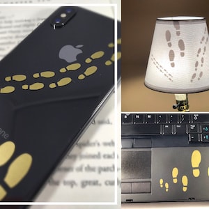 May include: Three different items with a gold footprint design. A black iPhone with the text "iPhone" on the back, a lampshade with a white background and a black laptop with a black keyboard.
