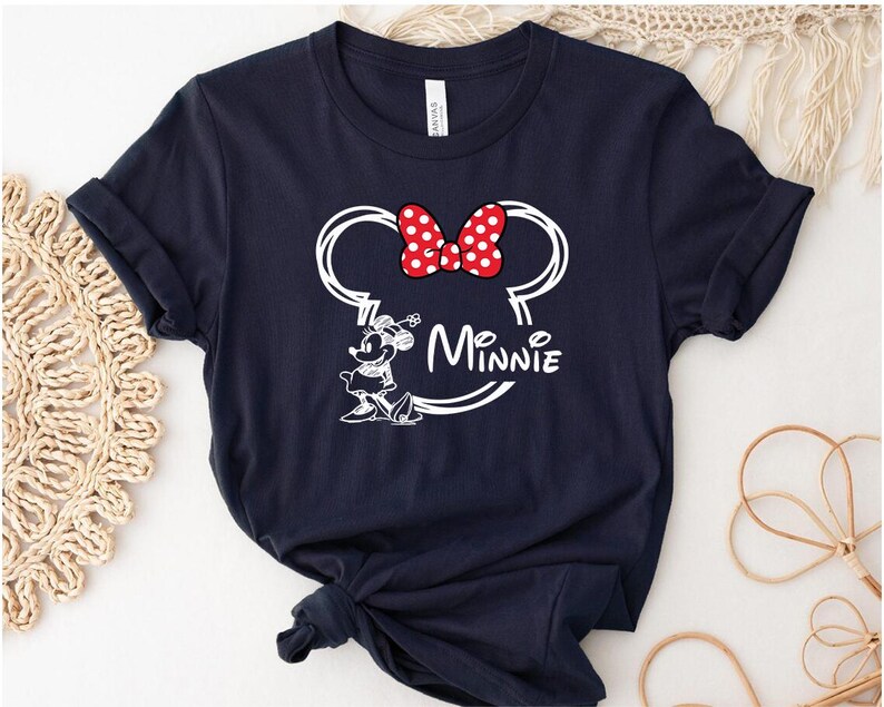 May include: A navy blue t-shirt with a white outline of Minnie Mouse's head and ears, a red bow with white polka dots, and the text "Minnie" underneath.