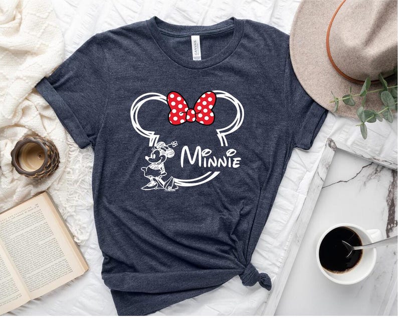 May include: A dark blue t-shirt with a white outline of Minnie Mouse's head and ears. The ears have a red bow with white polka dots. The text "Minnie" is written below the ears.