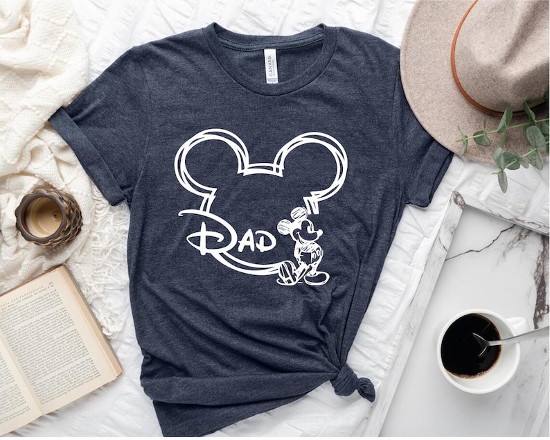 Pu&ograve; includere: Una maglietta blu scuro con un disegno bianco a forma di testa di Topolino e la parola "Pap&agrave;" all'interno delle orecchie.