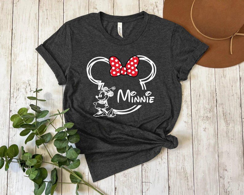 May include: A dark gray t-shirt with a white outline of Minnie Mouse's head and ears. The ears have a red bow with white polka dots. The text "Minnie" is written below the ears.