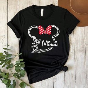 May include: Black t-shirt with a white outline of Minnie Mouse's head, a red bow with white polka dots, and the text "Minnie" underneath.