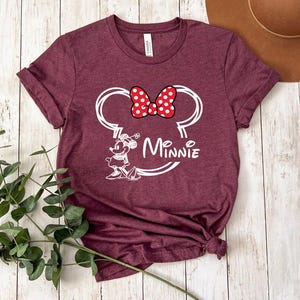 May include: Burgundy t-shirt with a white outline of Minnie Mouse's head and the word "Minnie" underneath. Minnie Mouse has a red bow with white polka dots.