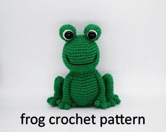 May include: Green crocheted frog amigurumi toy with black eyes and a white mouth.  The frog is sitting on a white surface.  frog crochet pattern