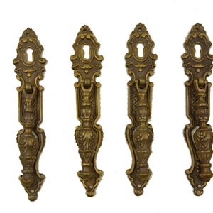 Könnte beinhalten: Vier antike Türgriffe aus Messing mit aufwendigen, floralen Designs. Jeder Griff hat oben ein Schlüsselloch und einen dekorativen Zug. Die Griffe haben eine warme, gealterte Messingfarbe, was auf Vintage-Hardware hindeutet.