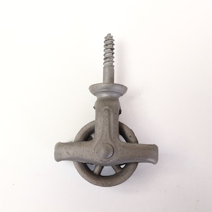Könnte beinhalten: Eine gusseiserne Umlenkrolle mit einer Gewindeschraube. Das Rad ist hellgrau und hat ein kreisförmiges Design mit Speichen. Die Schraube ist oben an der Umlenkrolle befestigt und ist etwa 5 cm lang.
