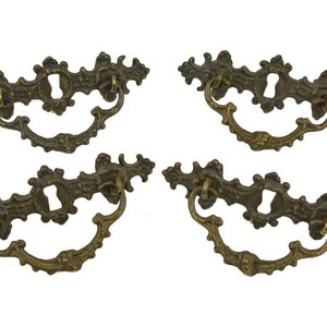 Könnte beinhalten: Satz von vier antiken Messing-Schrankgriffen mit verzierten Blumendesigns. Jeder Griff hat ein Schlüsselloch und einen gebogenen Griff.