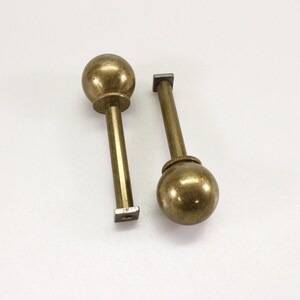 May include: Two gold-toned metal knobs with square bases. The knobs have a round, smooth top.