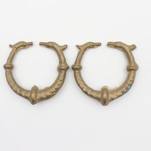 Puede incluir: Dos anillos de metal dorado con un diseño de delfín. Los anillos están abiertos y tienen una superficie lisa ligeramente texturizada.