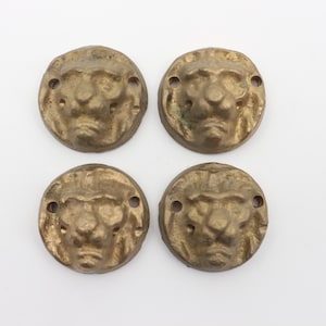 Può includere: Quattro bottoni in metallo color oro a forma di testa di leone con un design dettagliato. Ogni bottone ha due piccoli fori per il fissaggio.