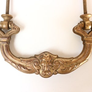 Könnte beinhalten: Ein goldfarbener Türgriff aus Metall mit verzierten Details und einem Rollendesign. Der Griff hat ein dekoratives, stilisiertes Blumenmuster und ein zentrales Motiv eines Löwenkopfes.