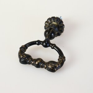 Könnte beinhalten: Schwarzer Metall-Schrankgriff mit einem Ringgriff und einem dekorativen Blumenknauf. Der Griff ist in Form von zwei Händen geformt, die einen Ring halten.