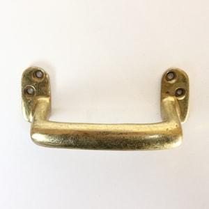 May include: A brass door handle with a rounded rectangular shape and two screw holes on each side.