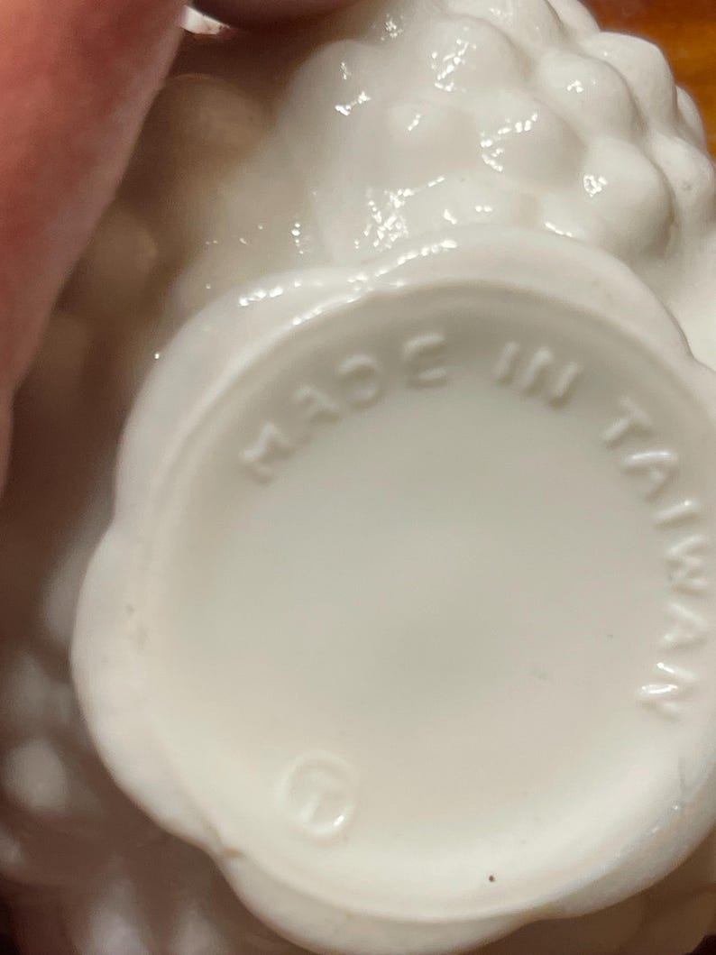 May include: A close-up of a white ceramic object with a textured surface. The base of the object has the words "MADE IN TAIWAN" stamped on it. The object has a scalloped edge.