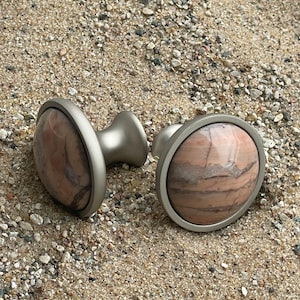 May include: Two round, silver-toned cabinet knobs with a brown and pink marbled stone inlay.