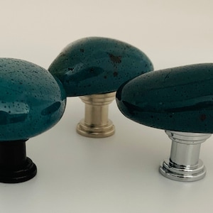 May include: Three teal blue ceramic cabinet knobs with different metal bases. The knobs are shaped like rounded pebbles.