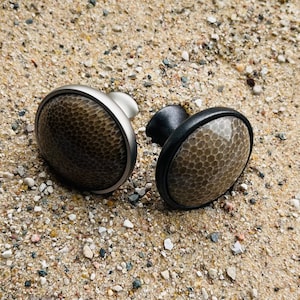 May include: Two round cabinet knobs with a textured, brown, leather-like finish. One knob has a silver base and the other has a black base.