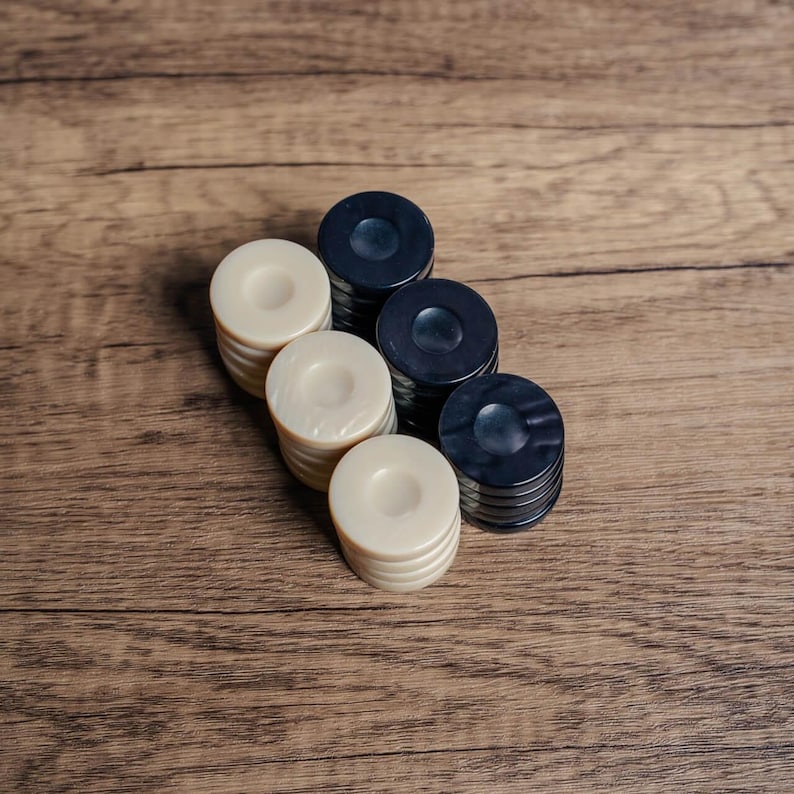 Puede incluir: Un conjunto de fichas de damas negras y blancas apiladas en una fila sobre una superficie de madera. Las fichas est&aacute;n dispuestas en colores alternos, con las fichas negras encima de las fichas blancas.