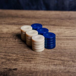 May include: A row of blue and white game counters stacked on a wooden surface. The counters are arranged in alternating colours, with the blue counters on the right and the white counters on the left.