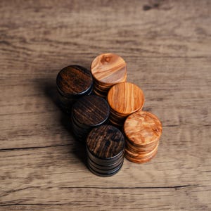 May include: A collection of six wooden bottle stoppers. The stoppers are round with a stacked design. The wood grain varies from light to dark brown. They are arranged on a wooden surface.