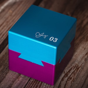 May include: A blue and purple puzzle box with the number "03" and a signature on the top.