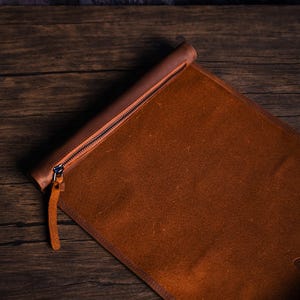 May include: A brown leather roll-up case with a zipper closure. The case is unrolled and lying flat on a wooden surface.