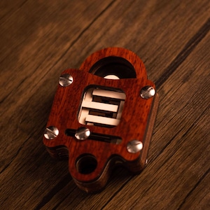 Op de afbeelding: Een houten puzzel in de vorm van een hangslot met een rood mahoniekleurige afwerking. De puzzel heeft een reeks in elkaar grijpende stukken die moeten worden gemanipuleerd om het slot te openen.