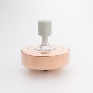 Könnte beinhalten: Eine kupferne Kreisel mit einer silbernen Spitze und einem gerändelten Knopf.