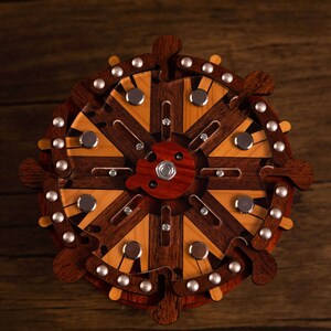 Puede incluir: Un rompecabezas de madera con un dise&ntilde;o circular. El rompecabezas tiene un centro con radios que irradian hacia afuera. Los radios est&aacute;n hechos de madera clara y oscura alternadas. El rompecabezas est&aacute; decorado con detalles met&aacute;licos plateados.