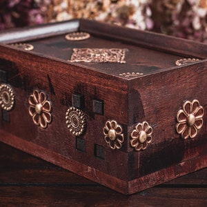 Puede incluir: Una caja de madera marrón oscuro con detalles decorativos de latón. La caja tiene un diseño floral y está cerrada.