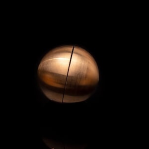 May include: A copper-colored sphere puzzle with a visible seam down the center, creating two halves. The puzzle is on a black background.