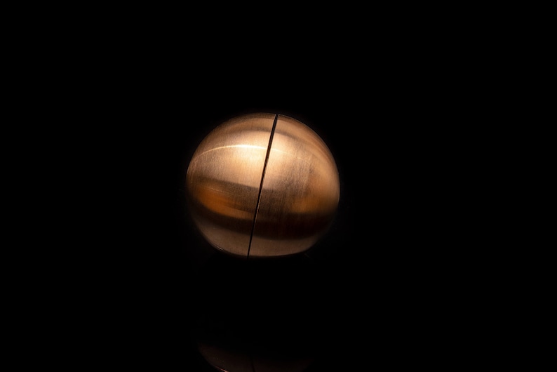 May include: A copper-colored sphere puzzle with a visible seam down the center, creating two halves. The puzzle is on a black background.