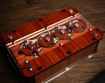 May include: A wooden box with a clear acrylic top revealing a complex, intricate gear mechanism. The box is made of dark red wood with a natural wood grain pattern.