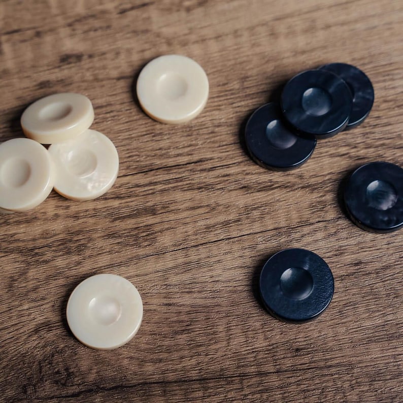 Puede incluir: Primer plano de una superficie de madera con fichas de juego negras y blancas. Las fichas negras est&aacute;n apiladas unas sobre otras, mientras que las fichas blancas est&aacute;n esparcidas.