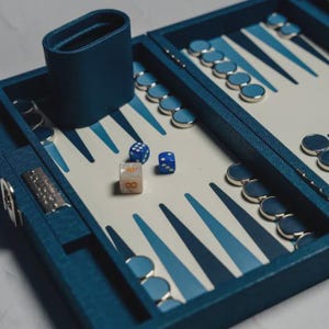 May include: A backgammon set with a blue leather case, dice cup, and game pieces. The board features a white and blue design. Three dice are visible, one with the number eight.