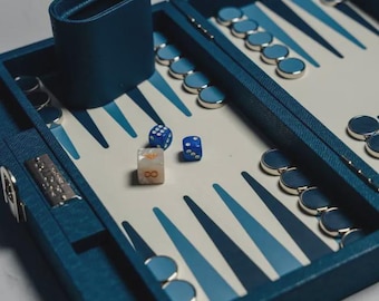 May include: A backgammon set with a blue leather case, dice cup, and game pieces. The board features a white and blue design. Three dice are visible, one with the number eight.