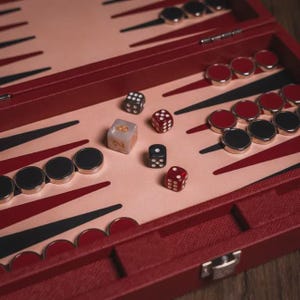May include: A close-up of a backgammon board with red and black accents. The board is open, revealing dice and game pieces. The dice are in various colors, and the game pieces are red and black. The board is made of wood.