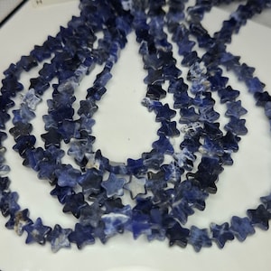 Könnte beinhalten: Eine Strähne aus blauen sternförmigen Edelsteinperlen. Die Perlen bestehen aus einem hellblauen und dunkelblauen Stein mit weißen Adern.