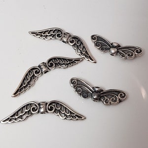 Pode incluir: Quatro pingentes de asa de anjo de metal prateado com detalhes intrincados. Os pingentes são de diferentes tamanhos e formas, e seriam perfeitos para adicionar um toque de fantasia a joias ou artesanato.